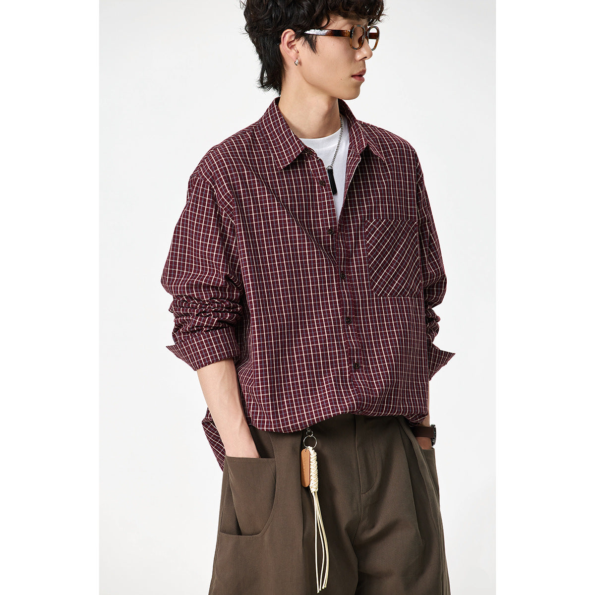 Close view of a model in a burgundy plaid button-up shirt with a diagonal-plaid chest pocket and brown trousers.