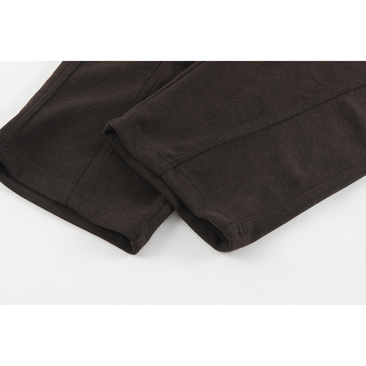 Close-up of the wide hems and stitching on dark brown trousers.