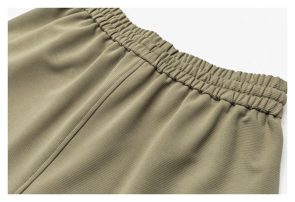Close-up of olive-khaki pants showing the gathered waistband and stitched seam.