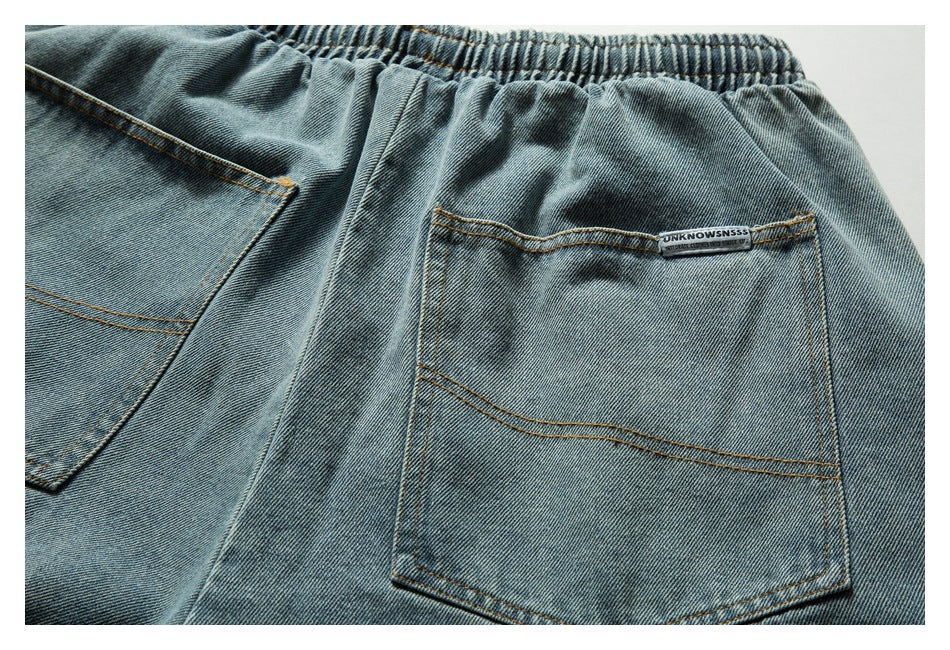 Back view of light blue denim shorts laid flat, showing two pockets, an elastic waistband, and a small sewn label.