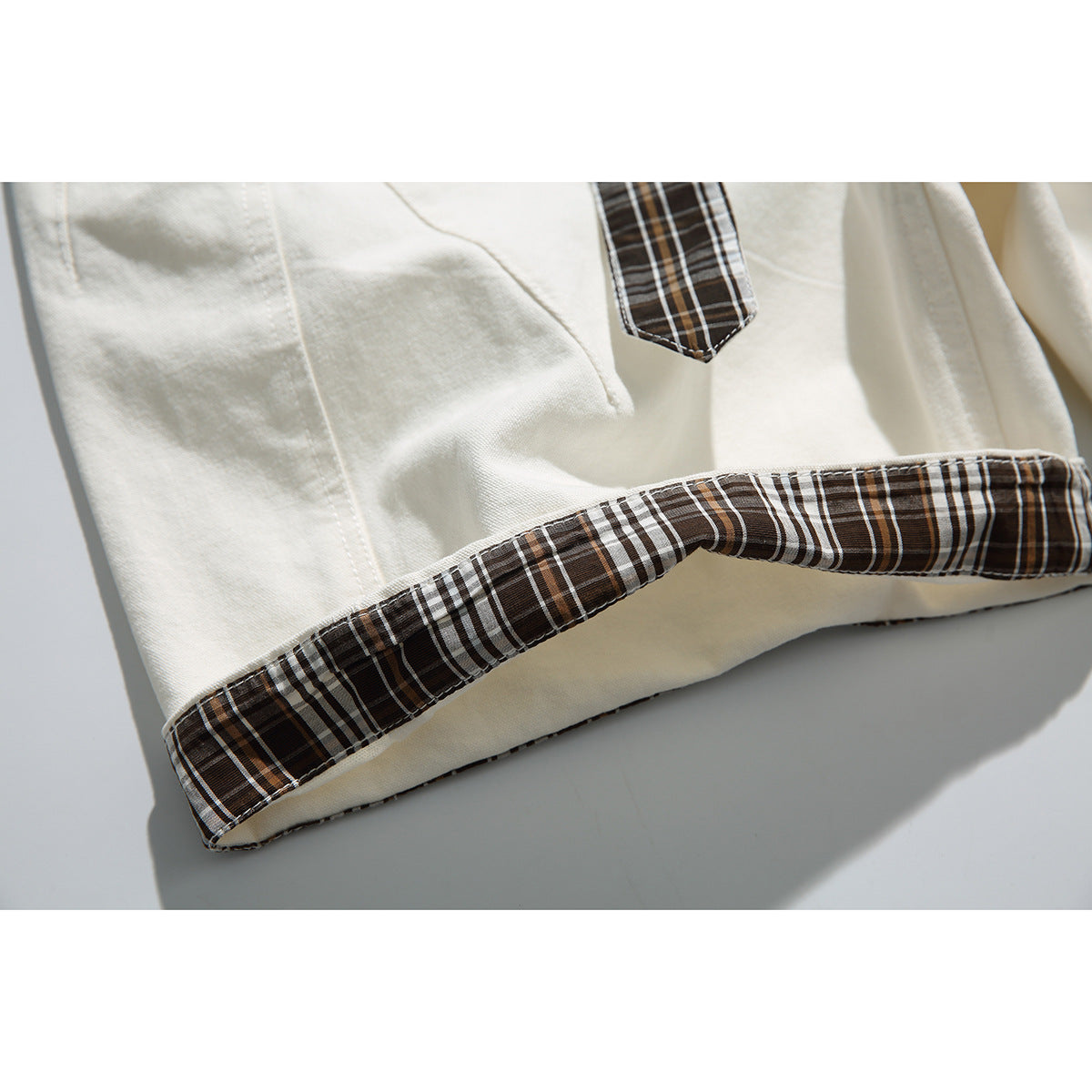 Close-up of the ivory shorts' turned-up hem, finished with dark brown, white, and tan plaid trim.