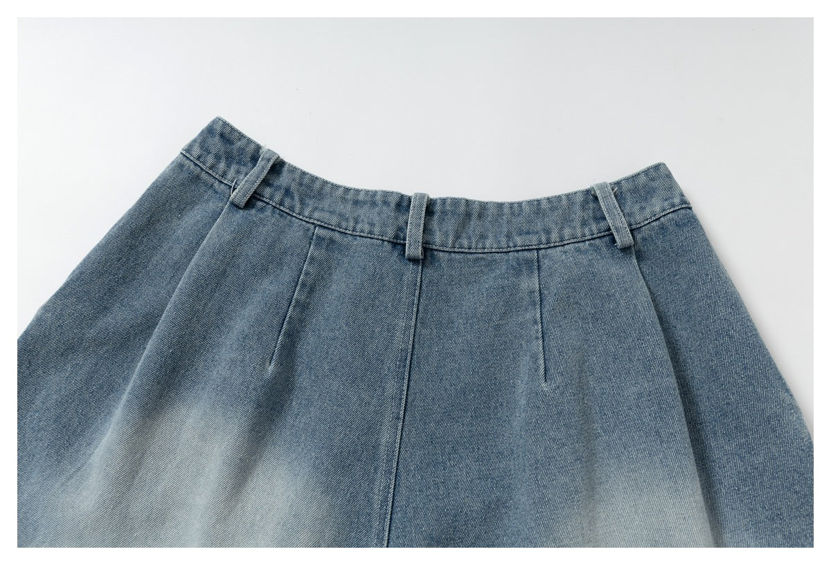 Cropped front view of blue denim trousers laid flat, showing the waistband, belt loops, and front pleats.