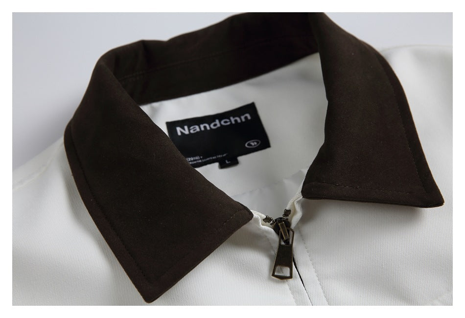 Close-up of a white garment's dark brown collar, front zipper, and black neck label.
