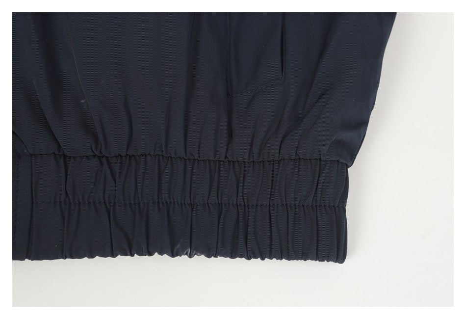 Close-up of the dark jacket's gathered elastic waistband and adjacent pocket seam.
