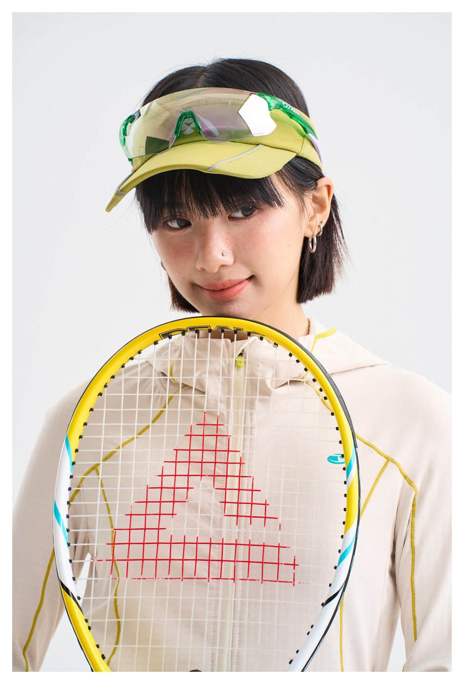 Close-up of a model wearing an ivory jacket, with a tennis racket in the foreground.