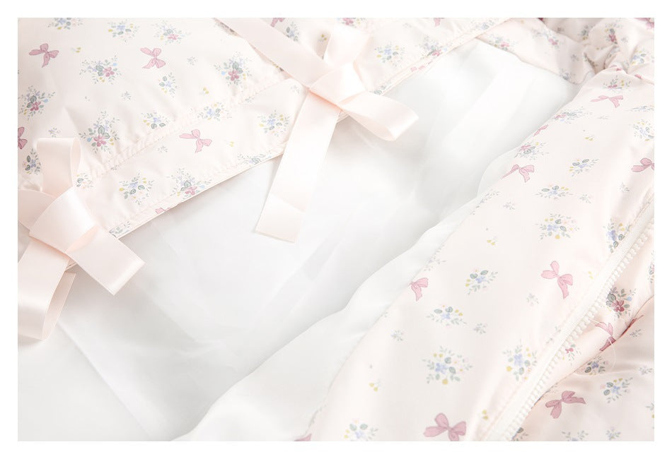 Close-up of a pale ivory floral-and-bow printed garment opening, tied with pink ribbons over a white inner panel.