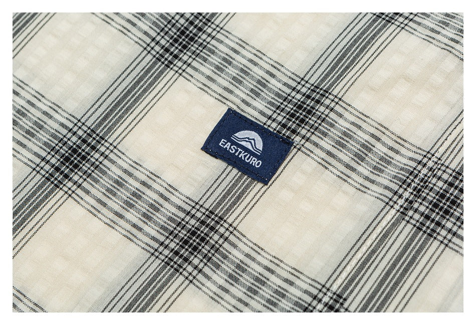 Close-up of an ivory-and-black plaid shirt with a small navy EASTKURO logo patch.