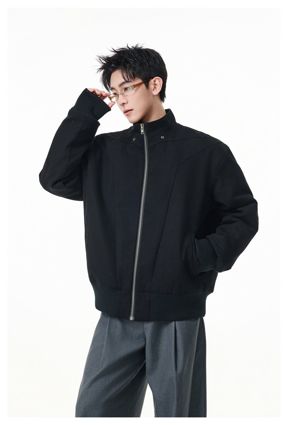 Model wearing a black stand-collar zip bomber-style jacket with ribbed cuffs and hem, with gray trousers