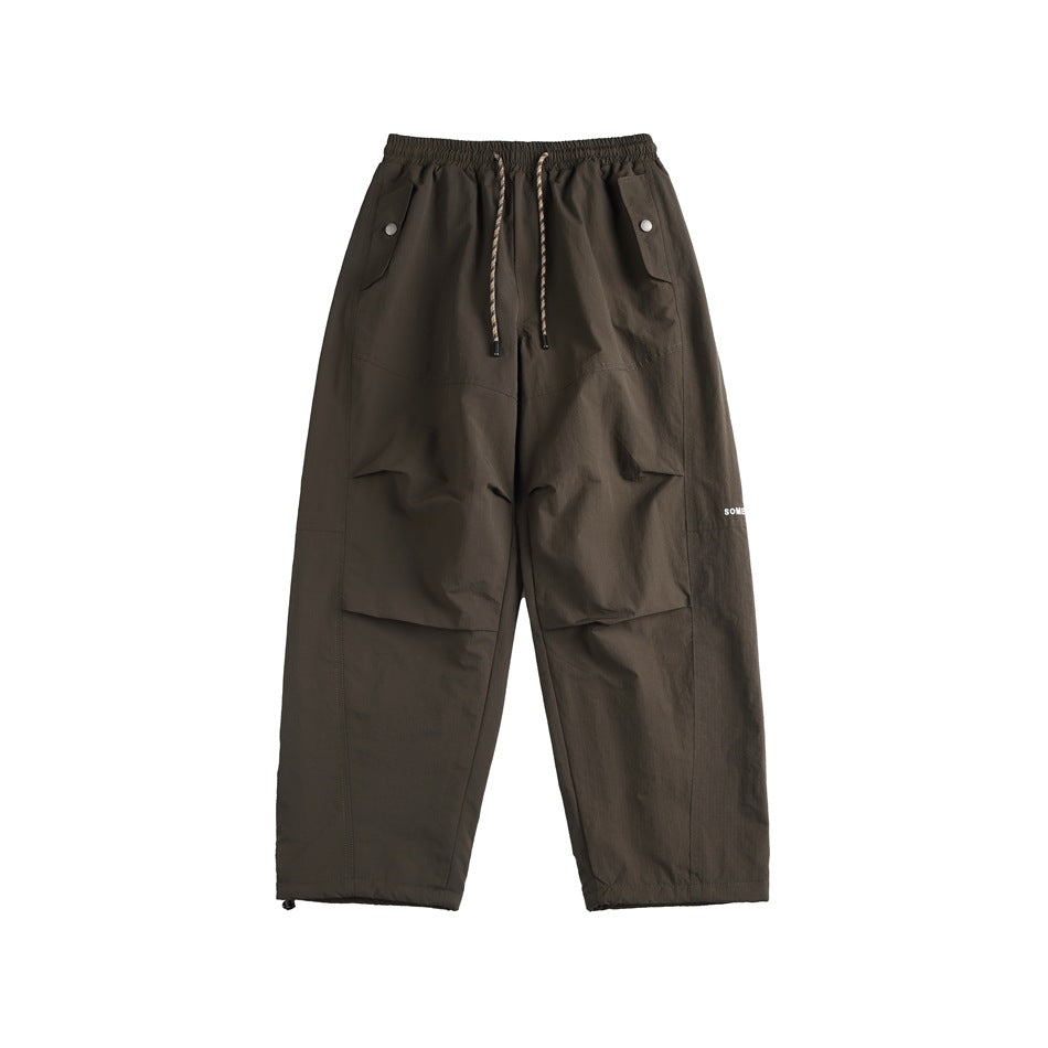 Dark brown wide-leg pants with rope drawstring, snap flap pockets and pleated knees, front flat lay