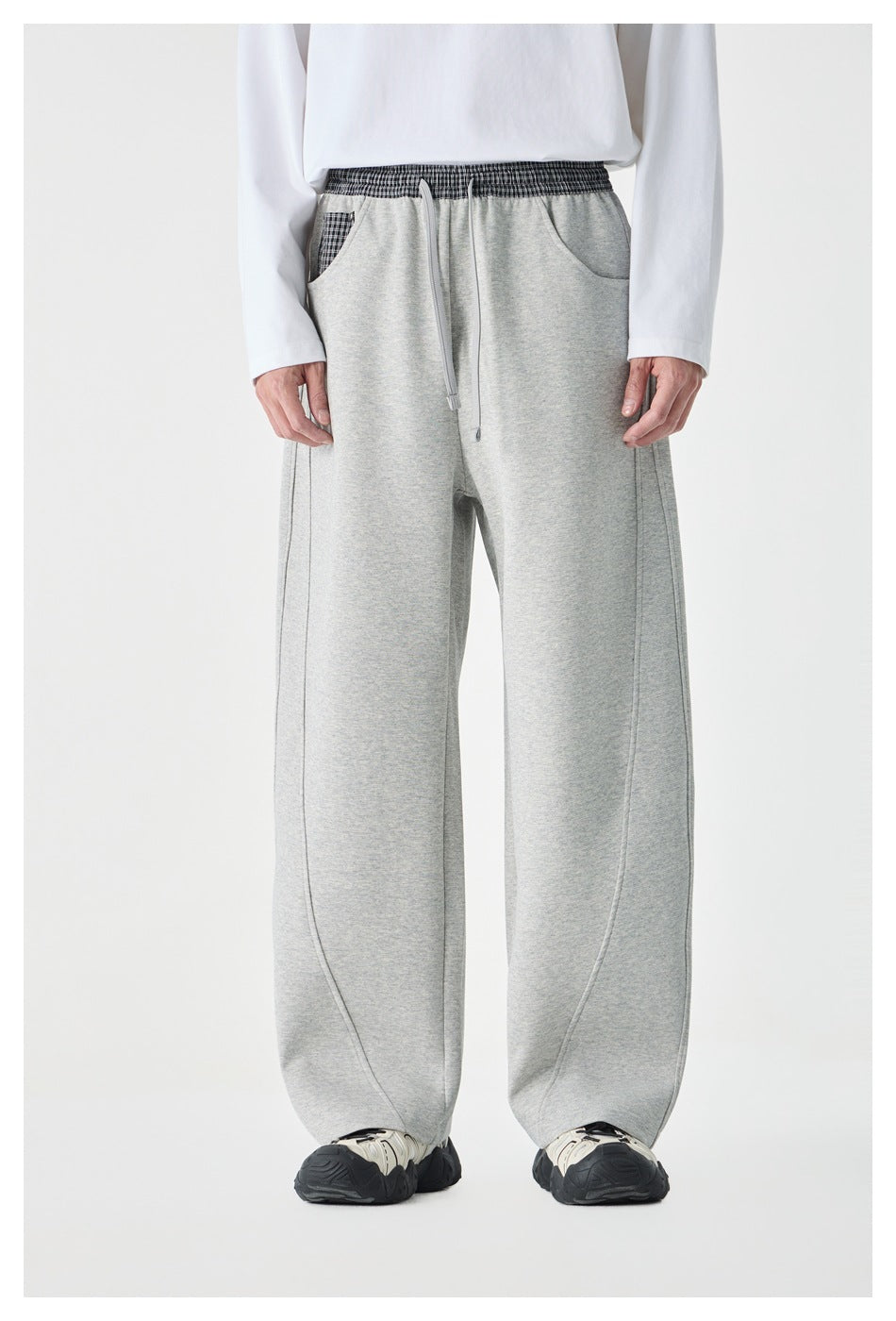 Person wearing gray wide-leg drawstring pants with plaid waistband, white long-sleeve top and chunky sneakers, front view