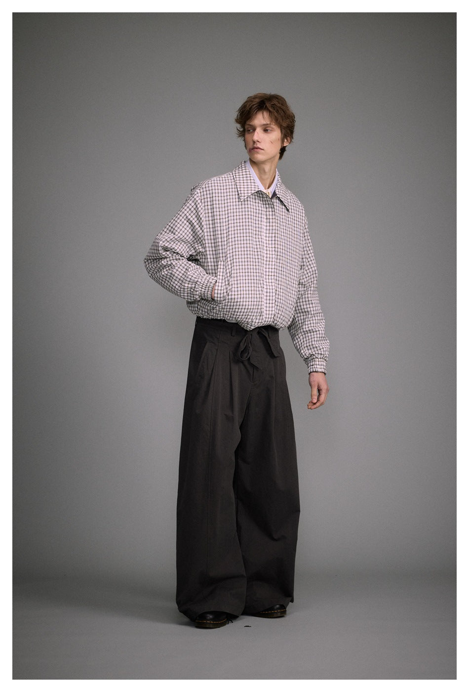Model in the zipped check jacket with one hand in the pocket, angled view with wide dark trousers