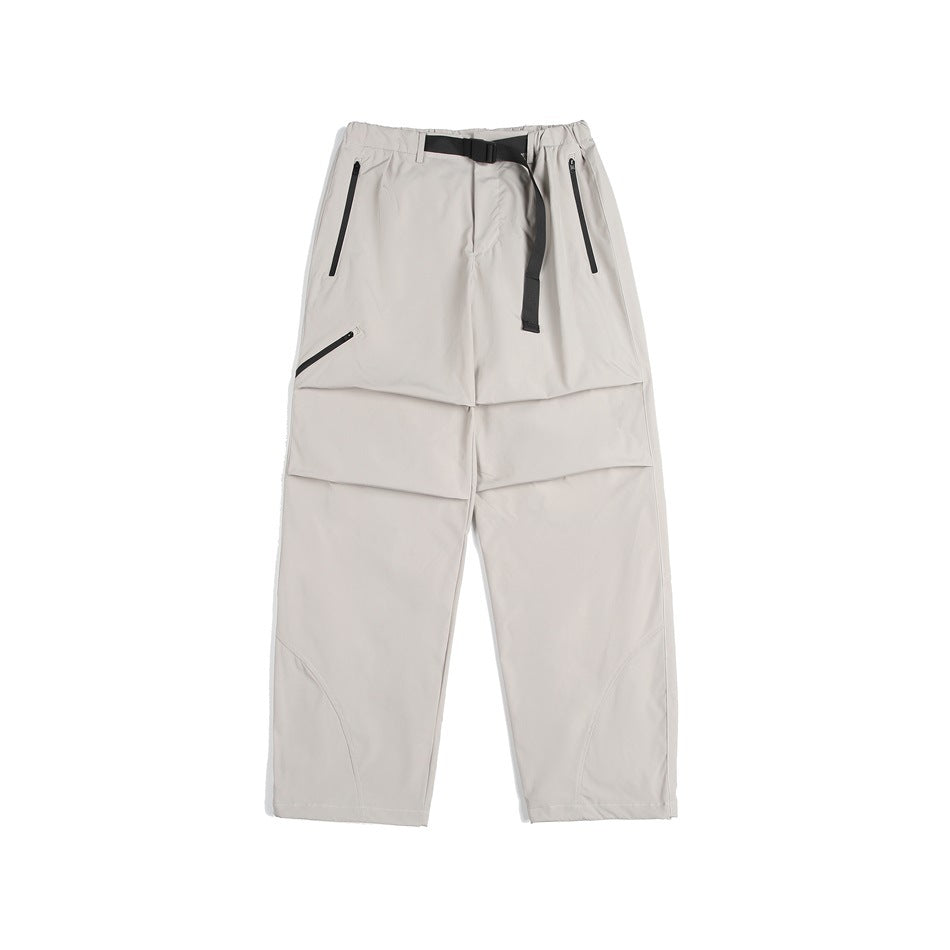 Light beige wide-leg pants with black belt, zippered pockets, knee pleats and curved lower-leg seams, flat lay
