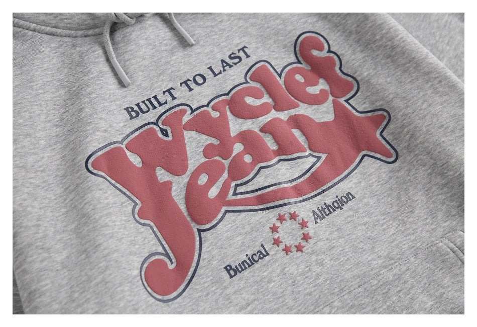 Close-up of a heather-gray hoodie’s raised red and navy chest graphic with stars and English lettering.