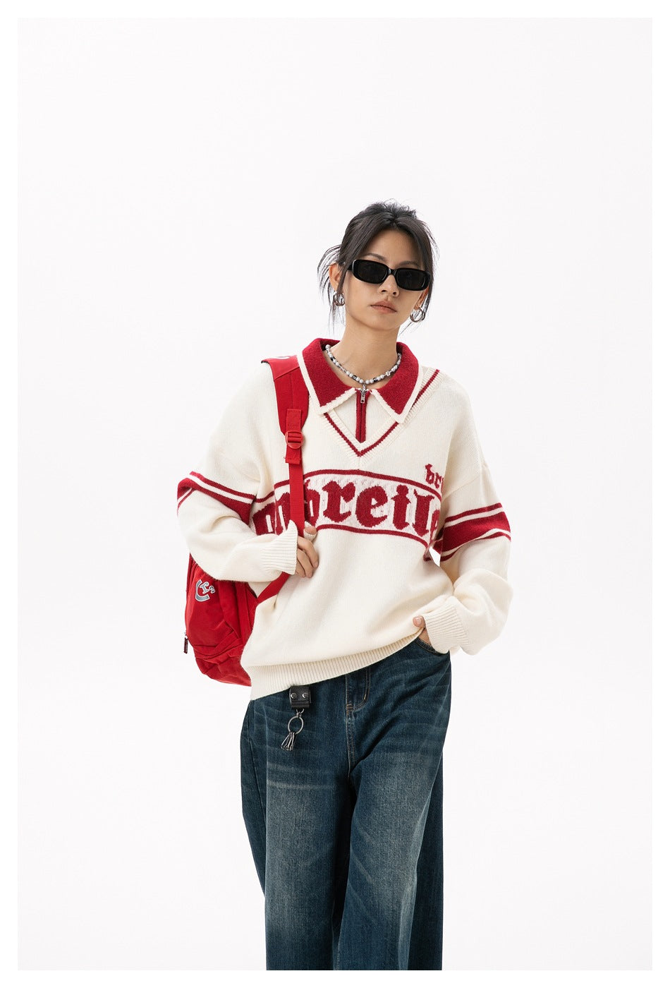 Closer view of a model wearing an ivory sweater with a red collar, sleeve stripes and large chest lettering.