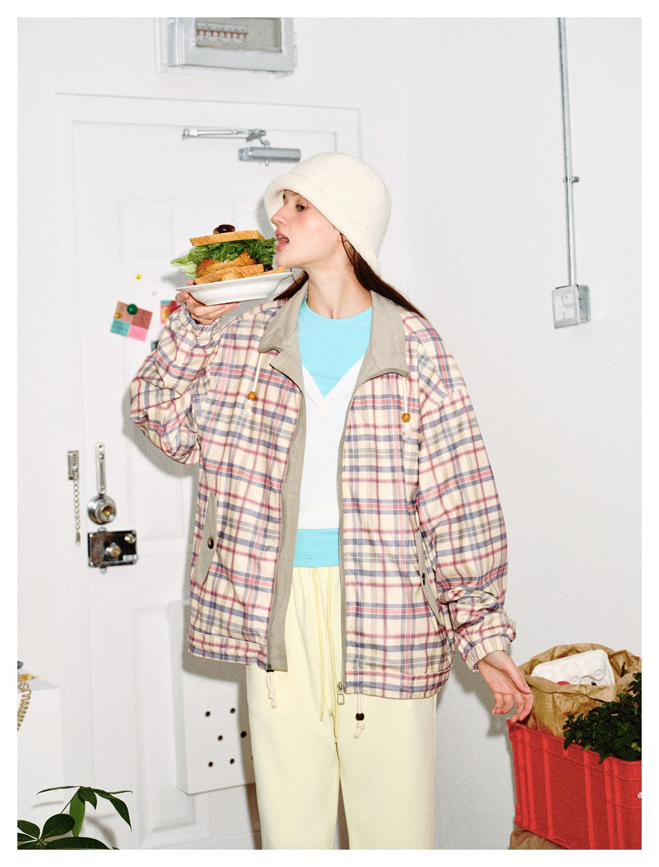 Model wearing plaid zip jacket with bead drawstrings and cream bucket hat, holding a sandwich plate