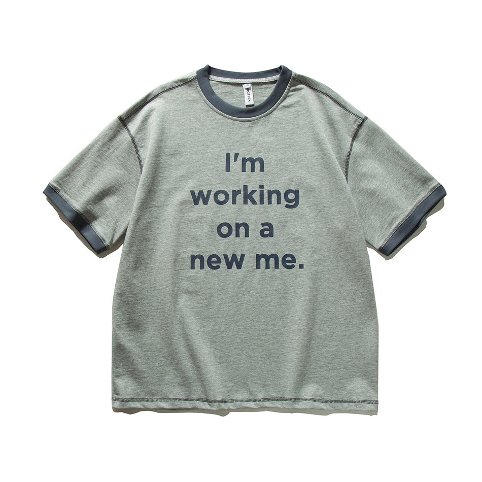 Gray-green short-sleeve T-shirt with dark slate trim and a dark "I'm working on a new me." slogan print on the front