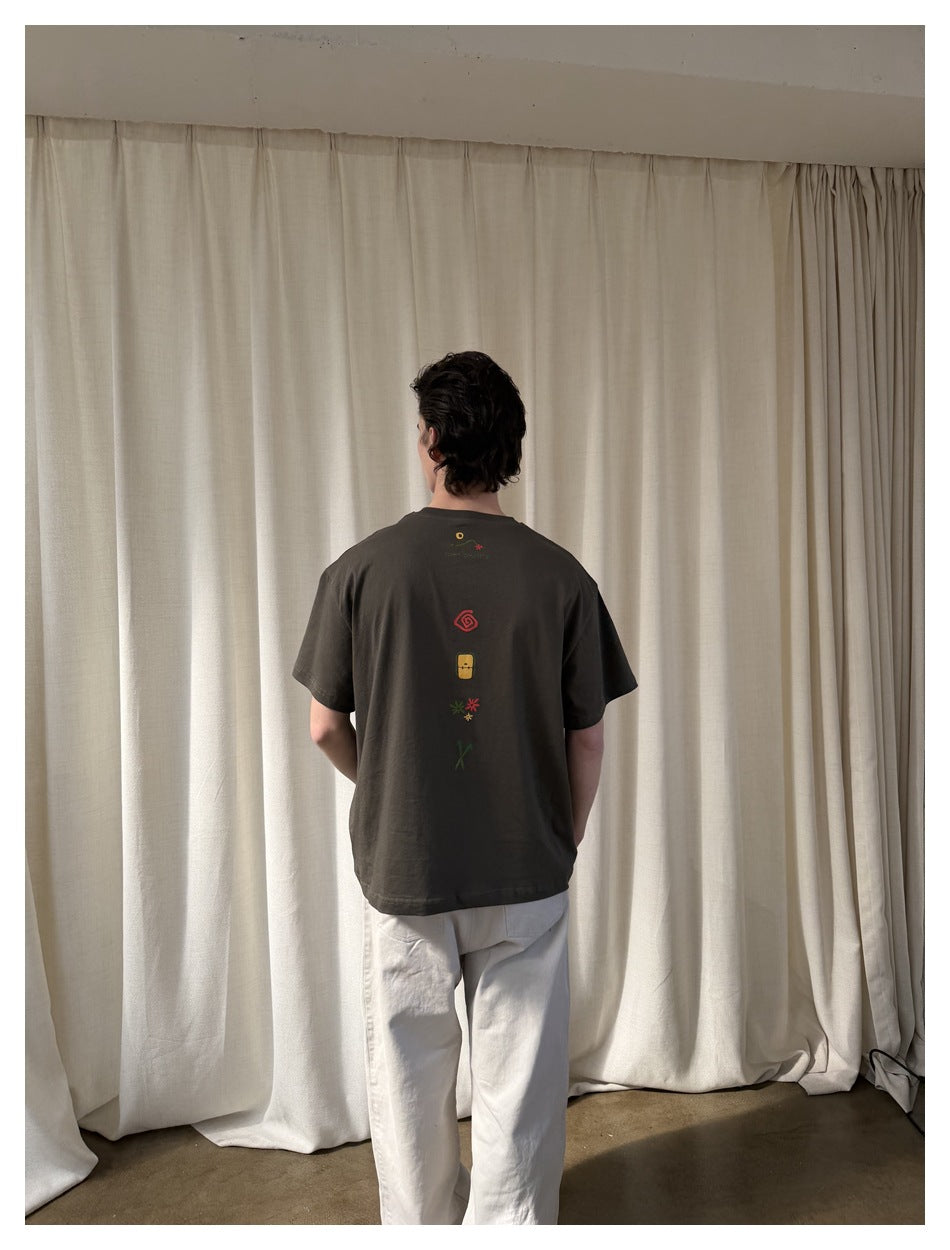 Back view of a model wearing a charcoal brown T-shirt with a vertical row of colorful graphics.