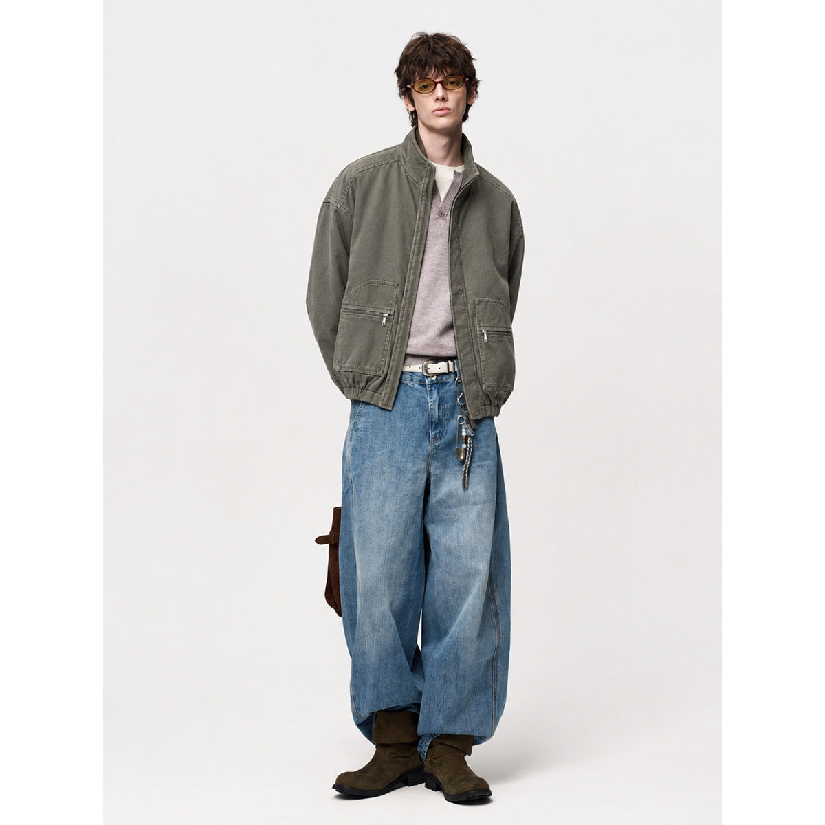 Model wearing an olive-gray zip jacket with large zip pockets and loose blue jeans.