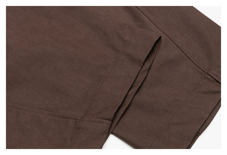 Close-up of dark brown trousers showing stitched panels and a narrow welt pocket opening.