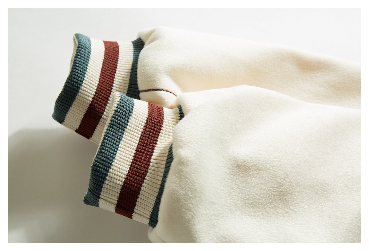Close-up of a cream jacket sleeve with ribbed cuffs striped in dark green, cream, and rust.