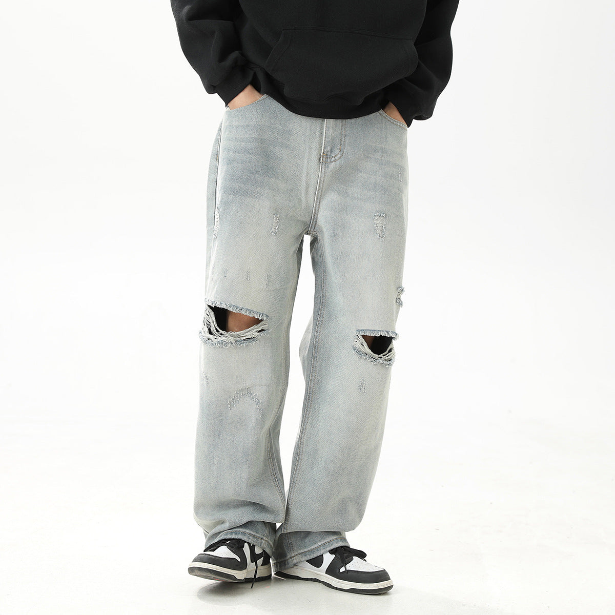 Model wearing loose, pale blue distressed jeans with large frayed knee holes, shown from the front.