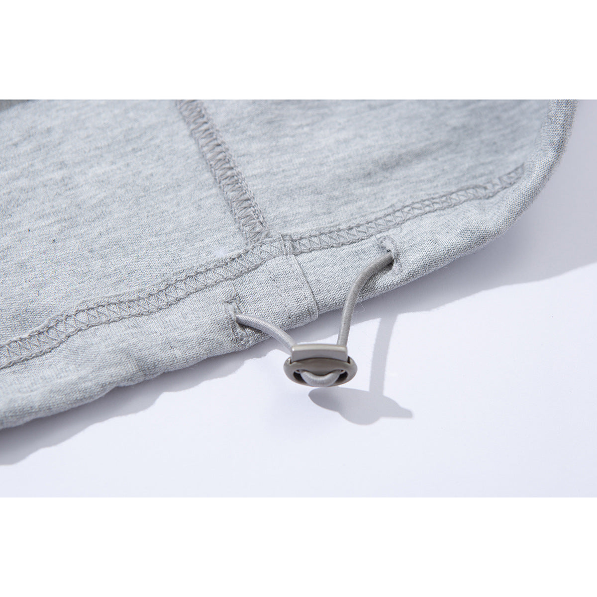 Close-up of the stitched hem and adjustable drawcord toggle on light gray sweatpants.
