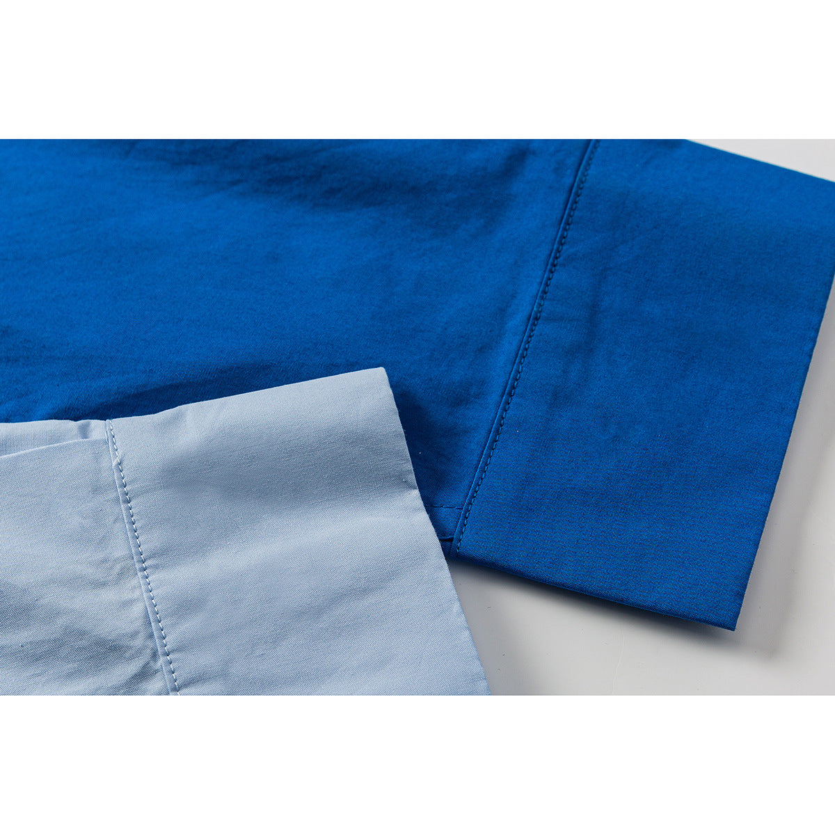 Close-up of a blue shirt sleeve beside a pale blue fabric panel, showing the seams and stitching.