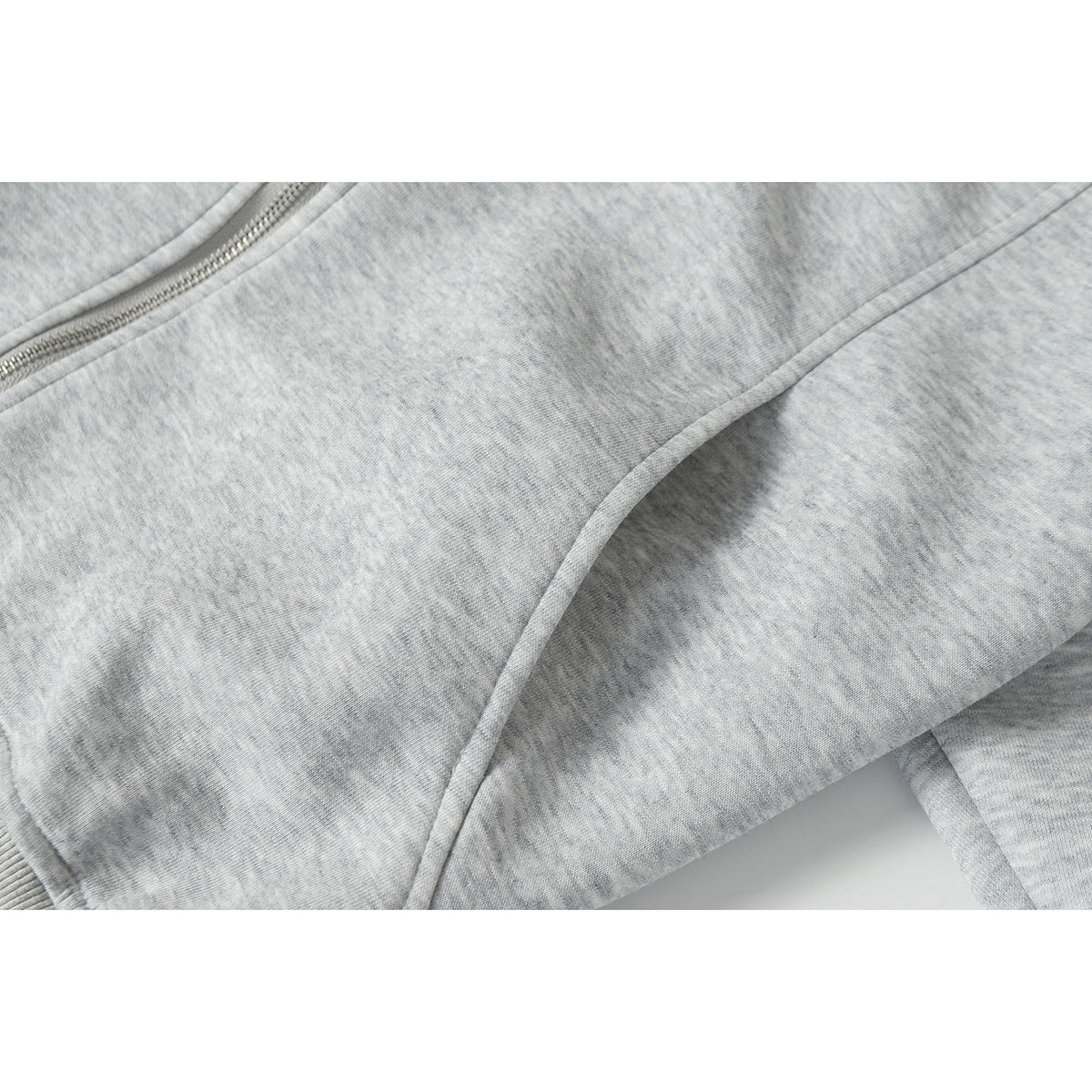 Close-up of light gray melange jacket fabric and curved stitched panel seam beside the zipper.