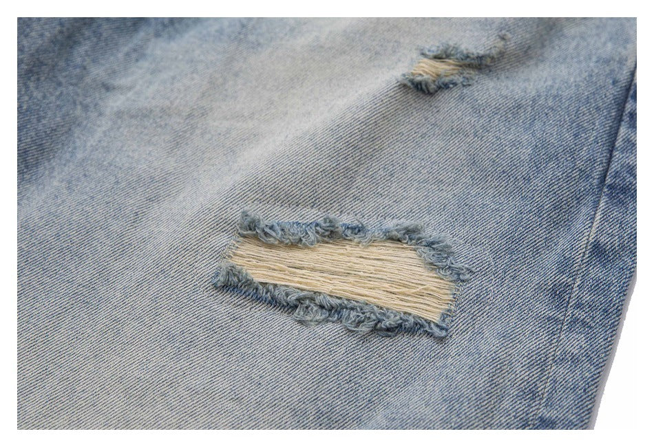 Close-up of a frayed horizontal tear with exposed threads in light-wash blue denim.
