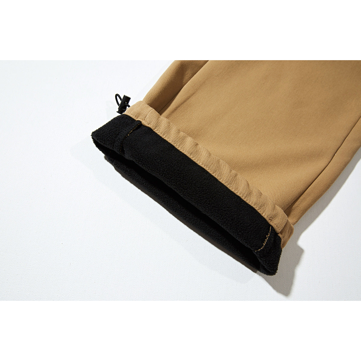Close-up of a tan pant cuff turned back to show black fleece lining and an adjustment cord.