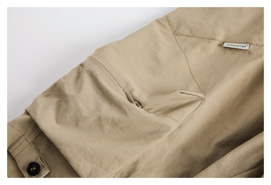 Close-up of a tan garment showing a buttoned cuff, stitched seams, a flap pocket, and a small sewn label.