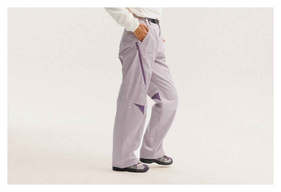 Three-quarter view of a model wearing light lavender trousers with a long purple side zipper and mesh knee accents.