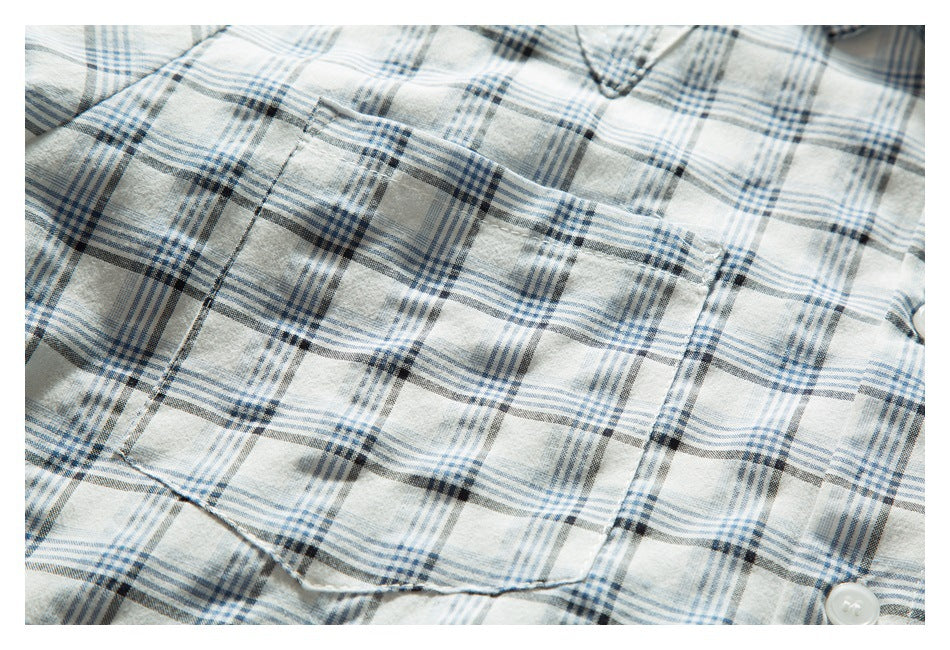 Close-up of white blue-and-charcoal plaid shirt fabric with a stitched pocket seam.