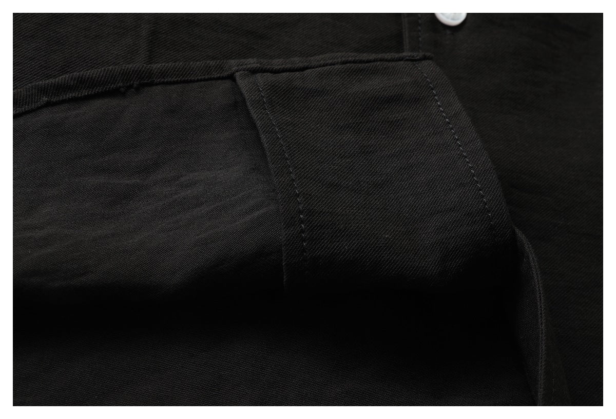 Close-up of a black garment's stitched panel and seam, with part of a white button visible.