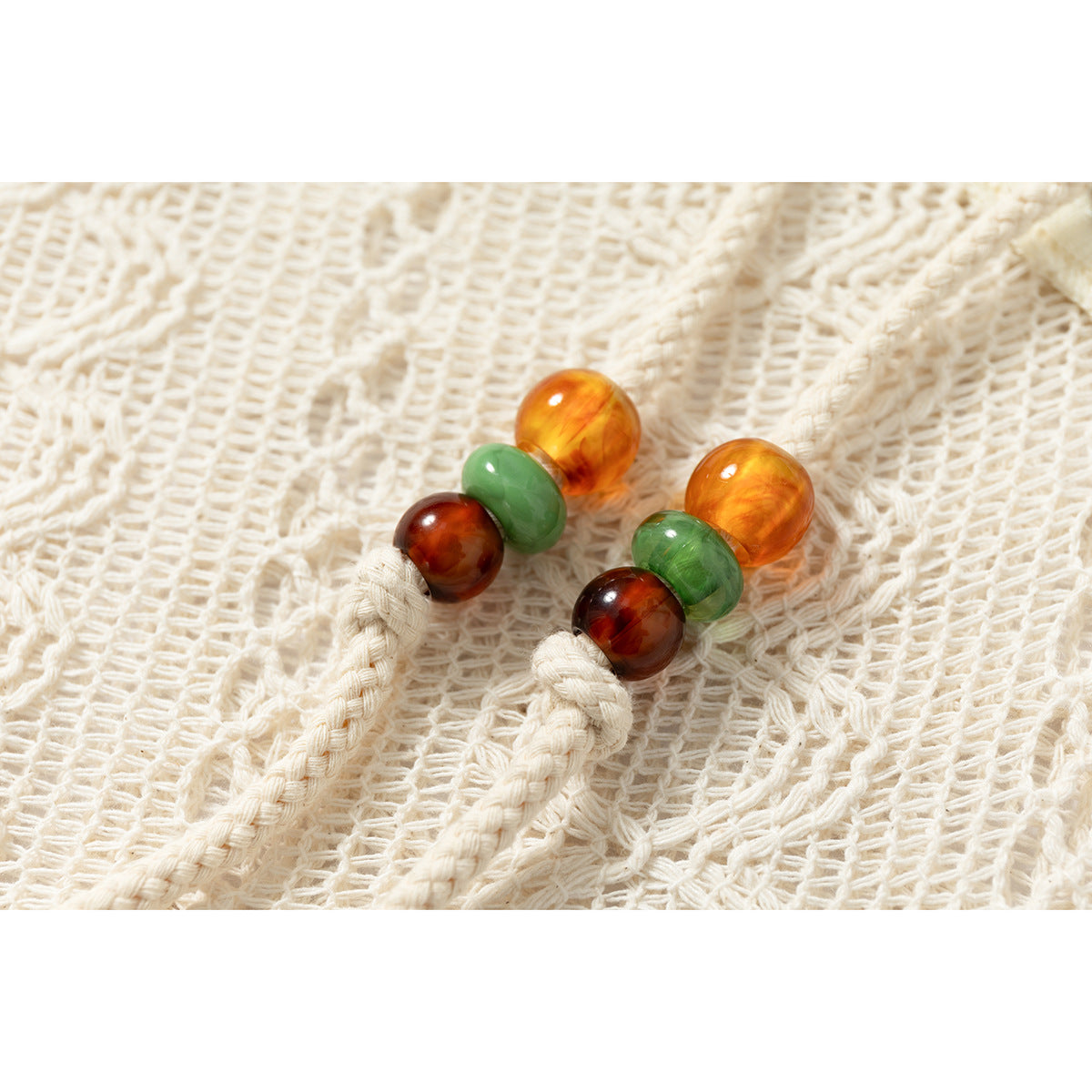 Close-up of two cream braided hoodie drawstrings with amber, green, and brown beads.