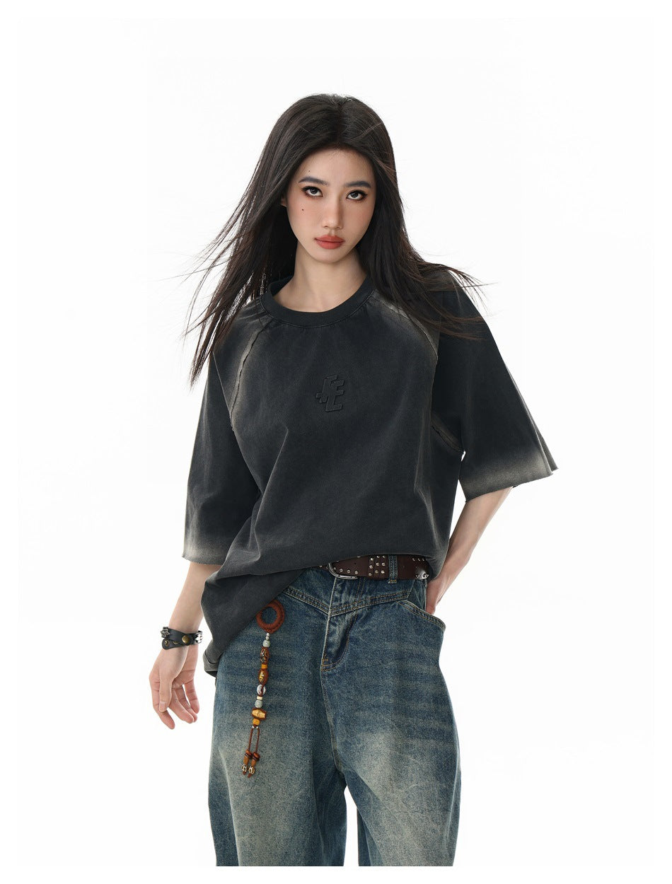 Model wearing an oversized charcoal T-shirt with faded gray accents and raglan seams, paired with loose blue jeans.