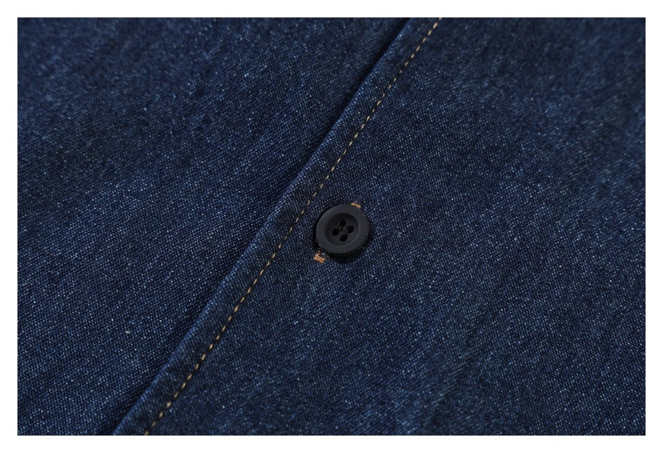 Close-up of a black button on dark indigo denim, beside a tan-stitched seam.