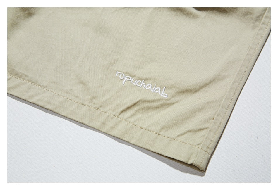 Close-up of white embroidered lettering near the hem of beige trousers.