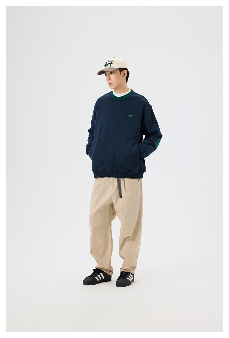 Front view of a model wearing a navy sweatshirt with green trim and rounded front pockets.
