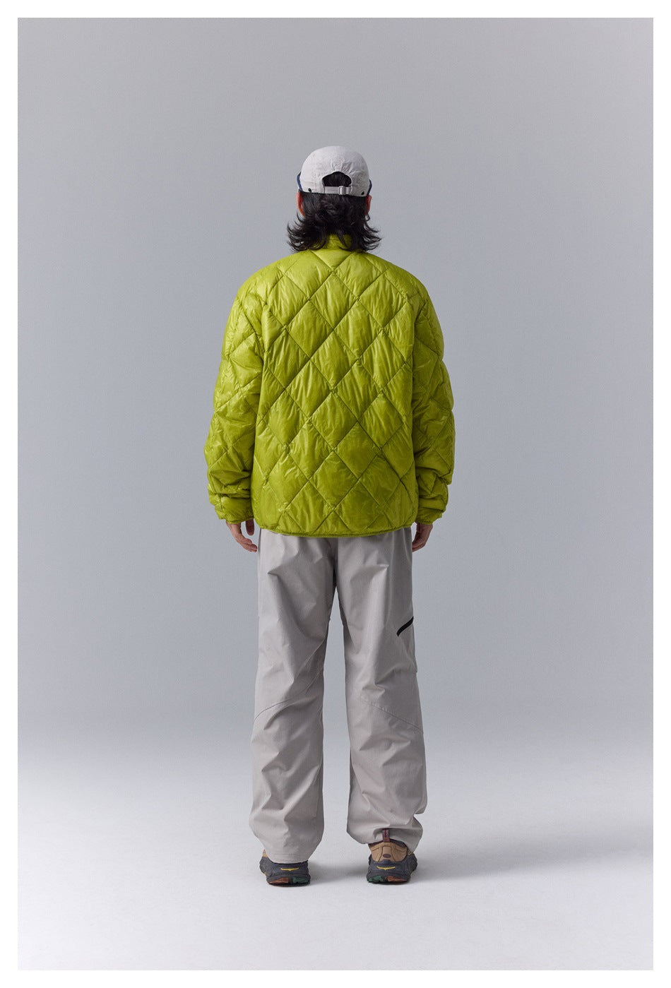 Rear view of a model wearing a lime-green quilted jacket with diamond stitching and light gray trousers.