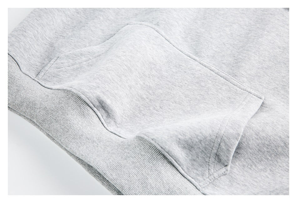 Close-up of a kangaroo pocket and ribbed waistband on a light heather-gray sweatshirt.