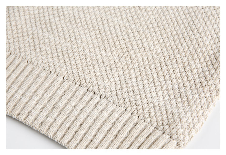 Close-up of the textured knit fabric and ribbed hem of a cream sweater.