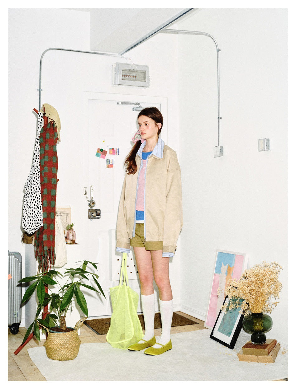 Model in a beige jacket with striped blue collar and cuffs, layered over a colorful top.