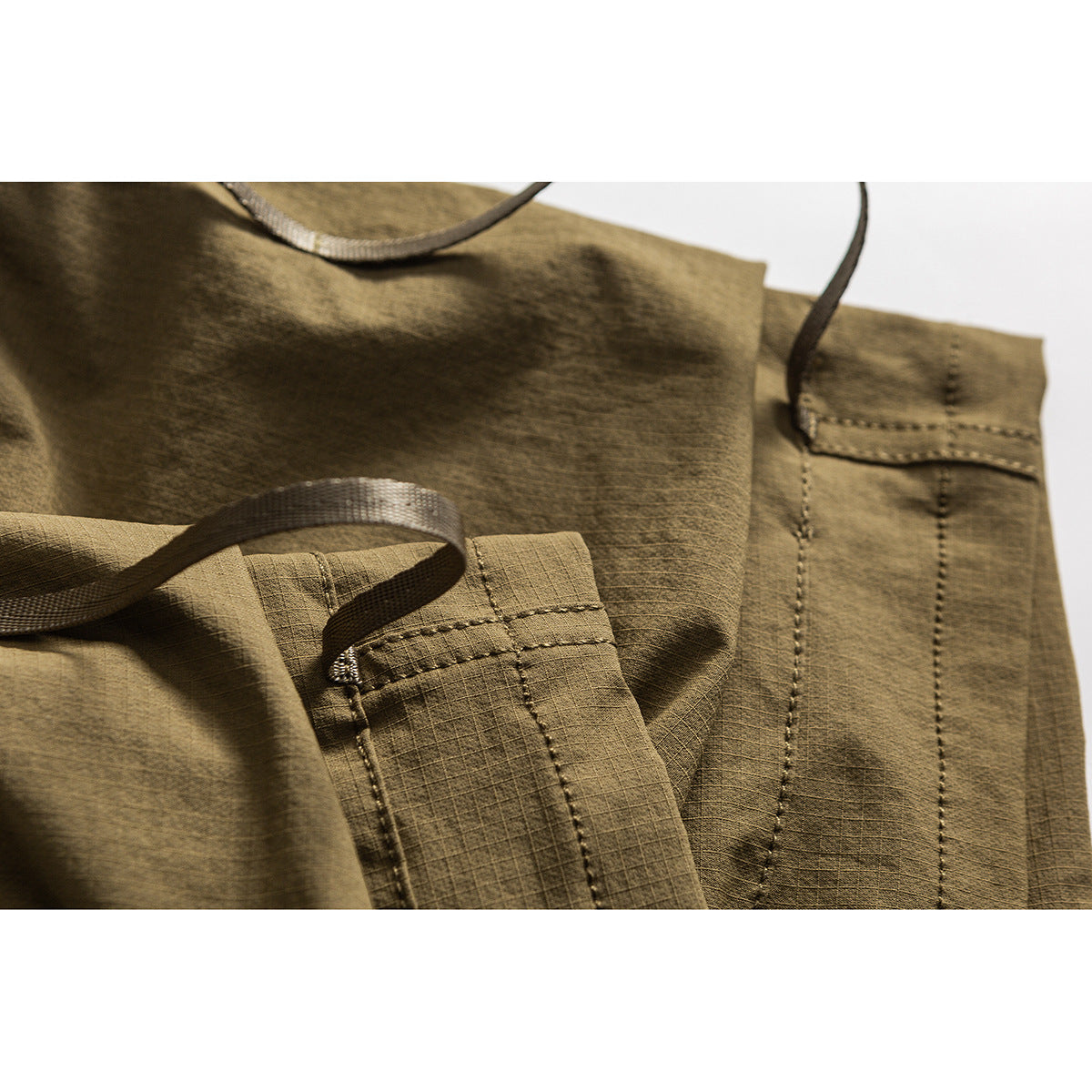 Close-up of olive cargo shorts with webbing loops, reinforced stitching, and pocket details.