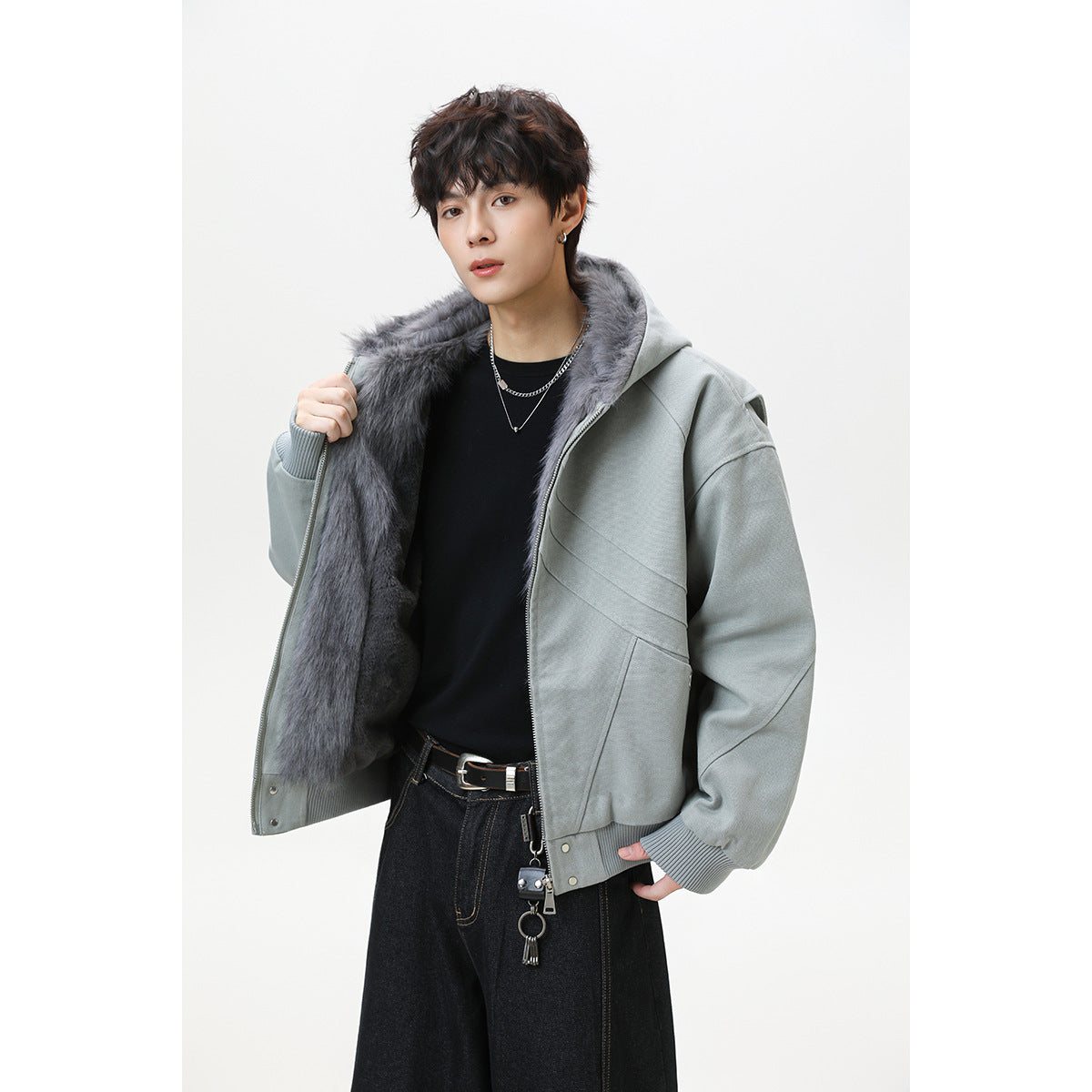 Model wears an open sage-gray hooded jacket with dark gray faux-fur lining and ribbed cuffs over a black shirt.
