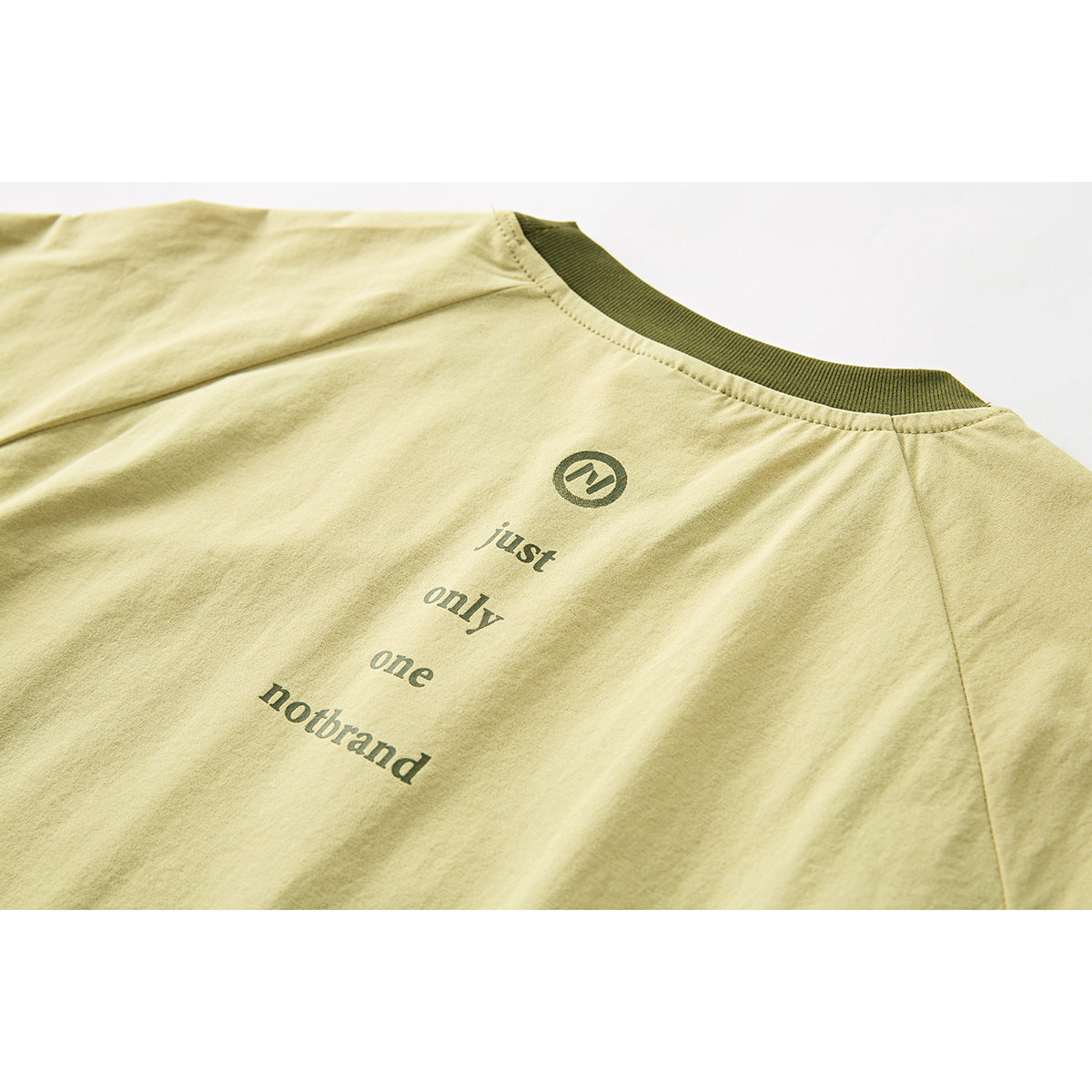 Close-up of a pale yellow-green T-shirt back with dark olive ribbed collar and centered English text print.