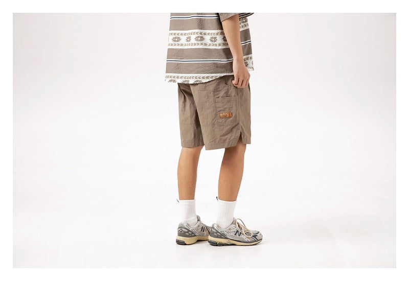 Side/rear view of a model wearing taupe knee-length shorts with a small patch and side slit.