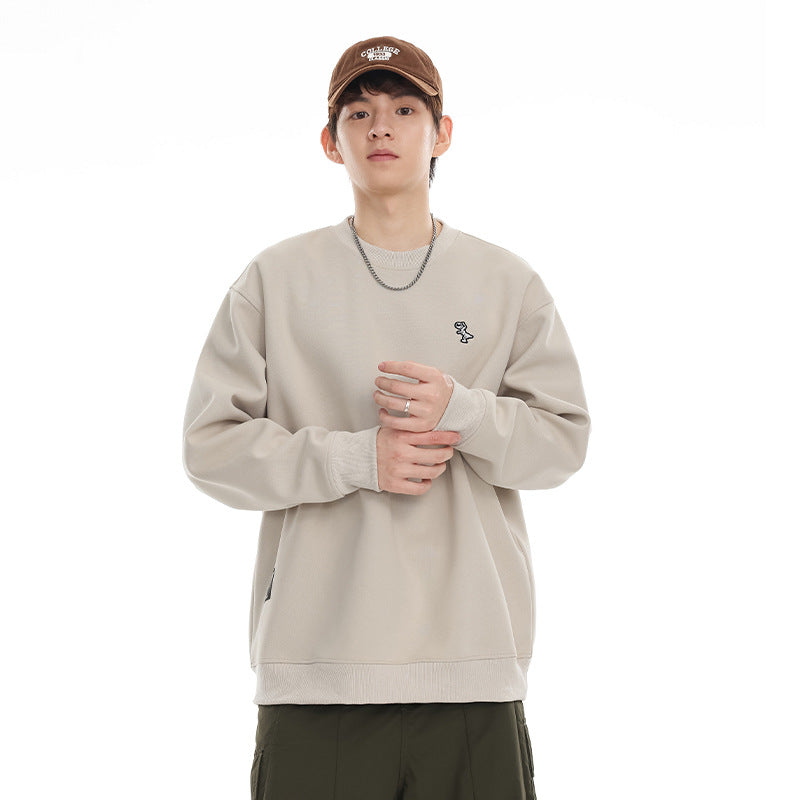 Model wearing a light beige crewneck sweatshirt with a small chest embroidery and ribbed cuffs and hem.