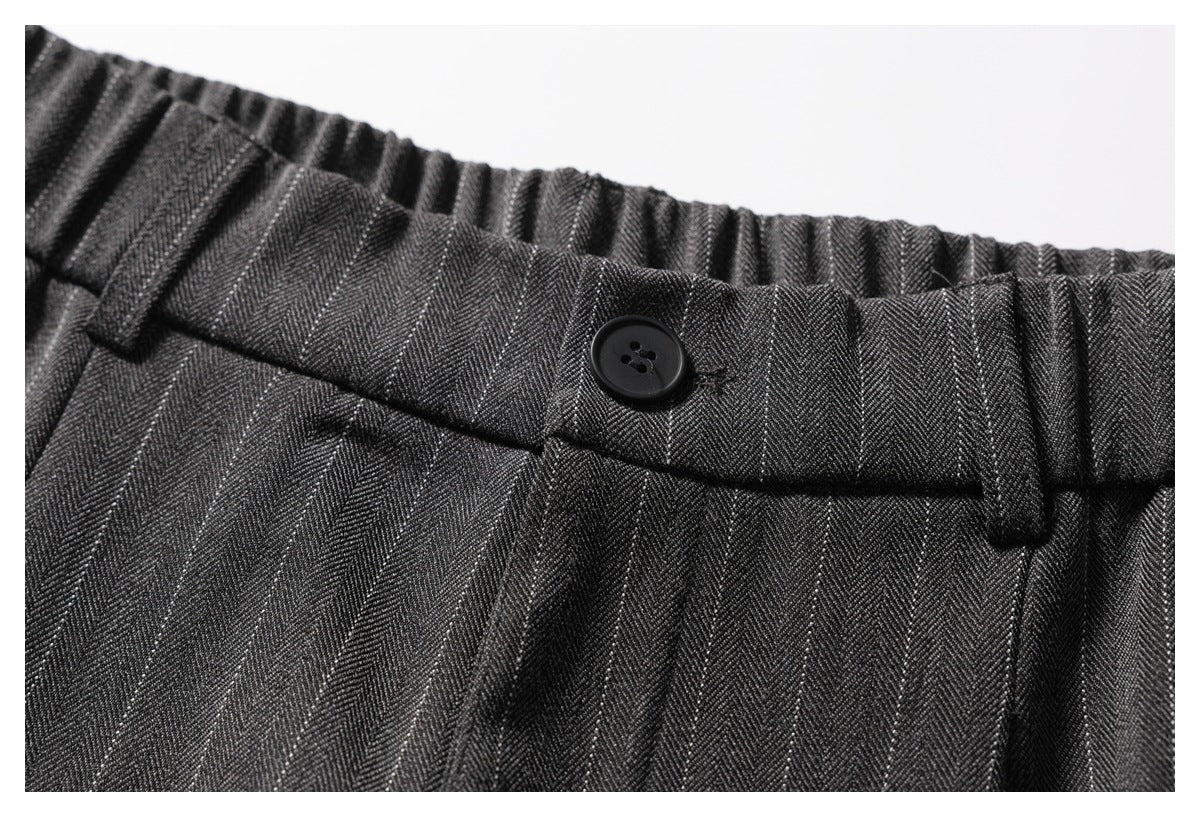 Close-up of charcoal pinstripe trousers showing the elasticated waistband, belt loops, and button closure.