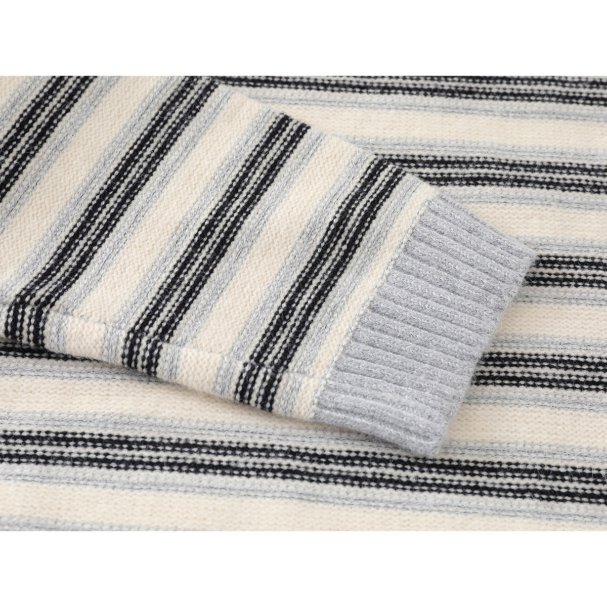 Close-up of a gray ribbed sweater cuff against cream, gray, and black striped knit.